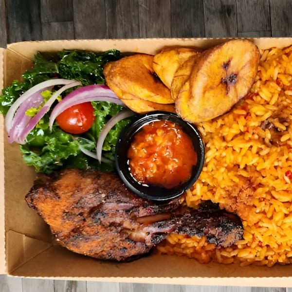 A BUKA New York takeout box with jollof rice, grilled chicken, plantains, salad, and sauce.