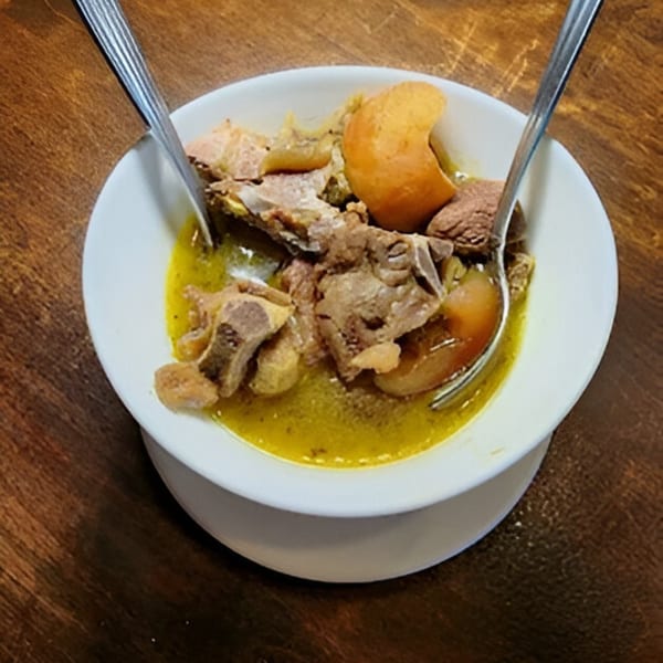 A white bowl of BUKA New York's African goat meat pepper soup with two spoons.