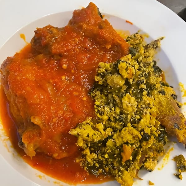 A plate of BUKA New York's African stewed chicken in red sauce with a side of green and yellow vegetables.