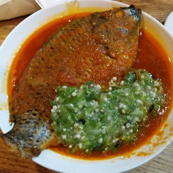 Whole fried fish in red stew with green okra soup, a dish from BUKA New York.