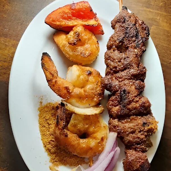 Grilled shrimp and meat skewers with red pepper, onions, and seasoning on a white plate.