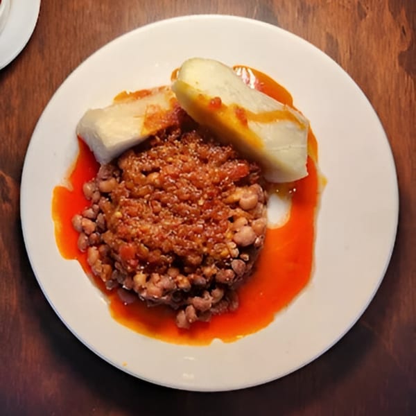 A white plate of BUKA New York's African beans and plantains in a red sauce.