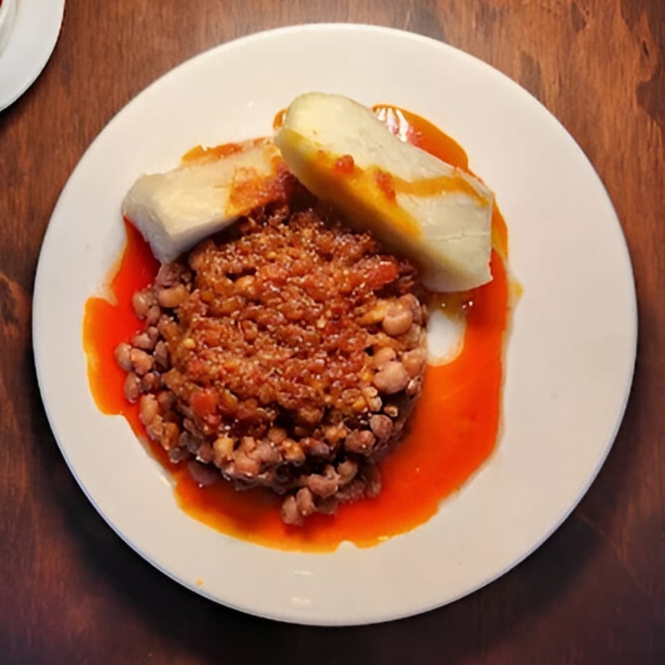 A white plate of BUKA New York's African beans and plantains in a red sauce.