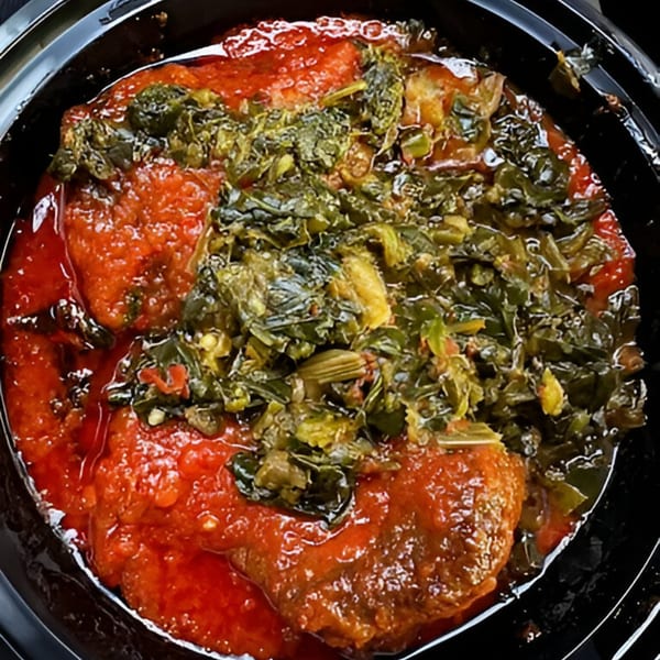 Close-up of BUKA New York's African stew with red sauce and green leafy vegetables.